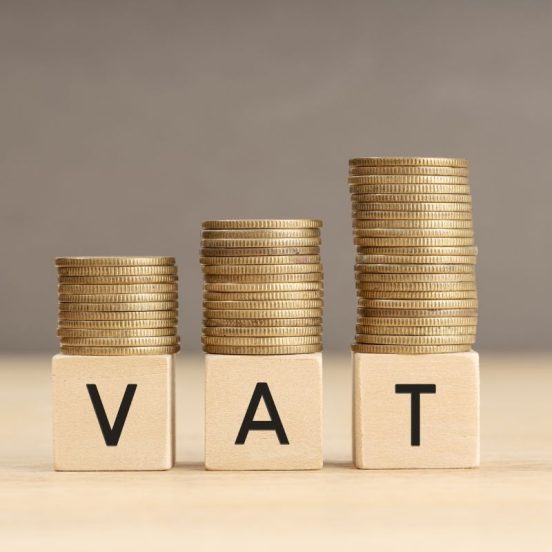 VAT word in wooden blocks with coins stacked in increasing stacks. Vat increasing concept. Copy space