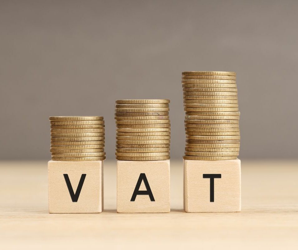 VAT word in wooden blocks with coins stacked in increasing stacks. Vat increasing concept. Copy space
